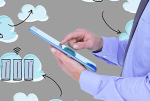 Gros plan sur les mains d'un homme en costume qui utilise une tablette, avec des icônes représentant le cloud qui gravitent autour.