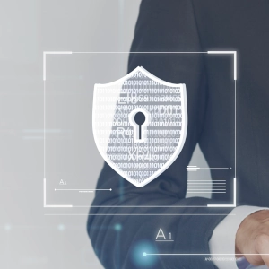 En arrière plan on voit le corps d'un homme en costume qui utilise une tablette tactile. Au premier plan, on aperçoit le symbole du bouclier qui fait ici référence à la cyberassurance.
