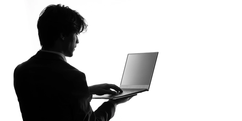 Une photo en noir et blanc d'un homme de 3/4 de dos qui utilise un ordinateur portable pour représenter la shadow IT.
