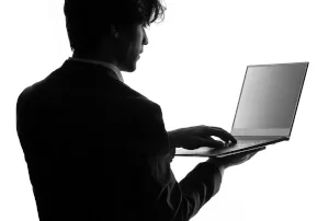 Une photo en noir et blanc d'un homme de 3/4 de dos qui utilise un ordinateur portable pour représenter la shadow IT.
