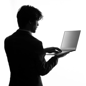Une photo en noir et blanc d'un homme de 3/4 de dos qui utilise un ordinateur portable pour représenter la shadow IT.